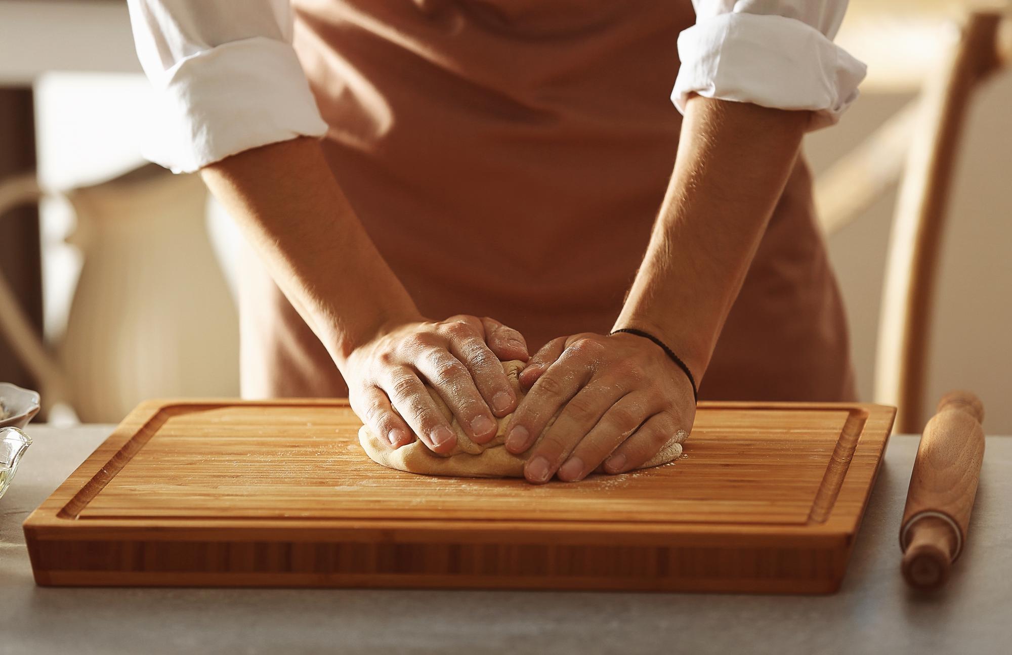 Hands kneading dough on wooden board